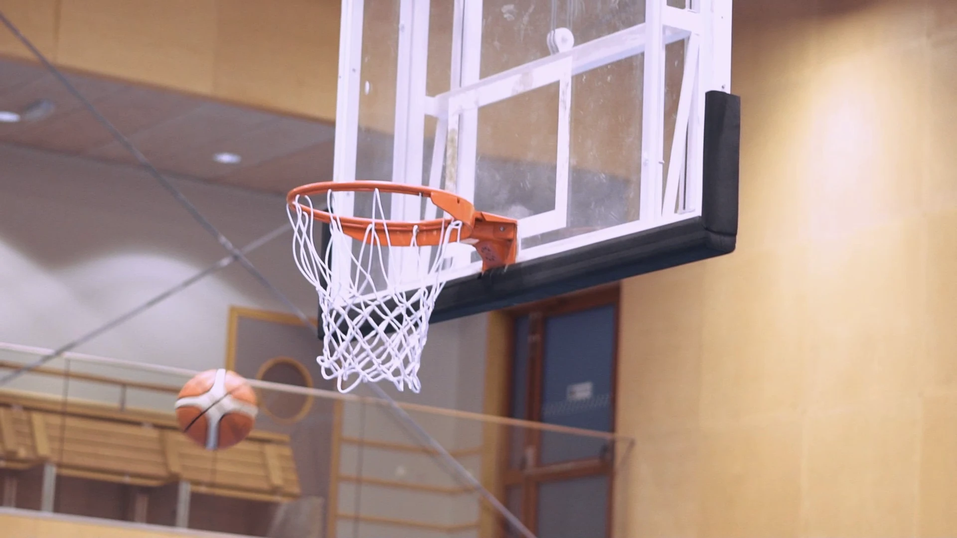 En basketkorg i en idrottshall, med en boll i luften bredvid.