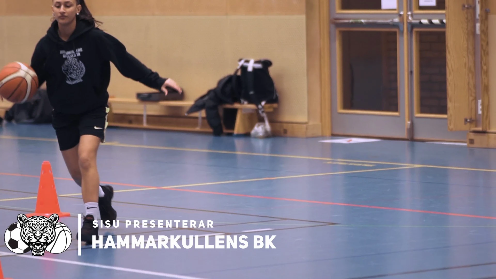 En basketspelare dribblar mellan koner i en idrottshall, med texten ”SISU presenterar Hammarkullens BK” och klubbens märke.
