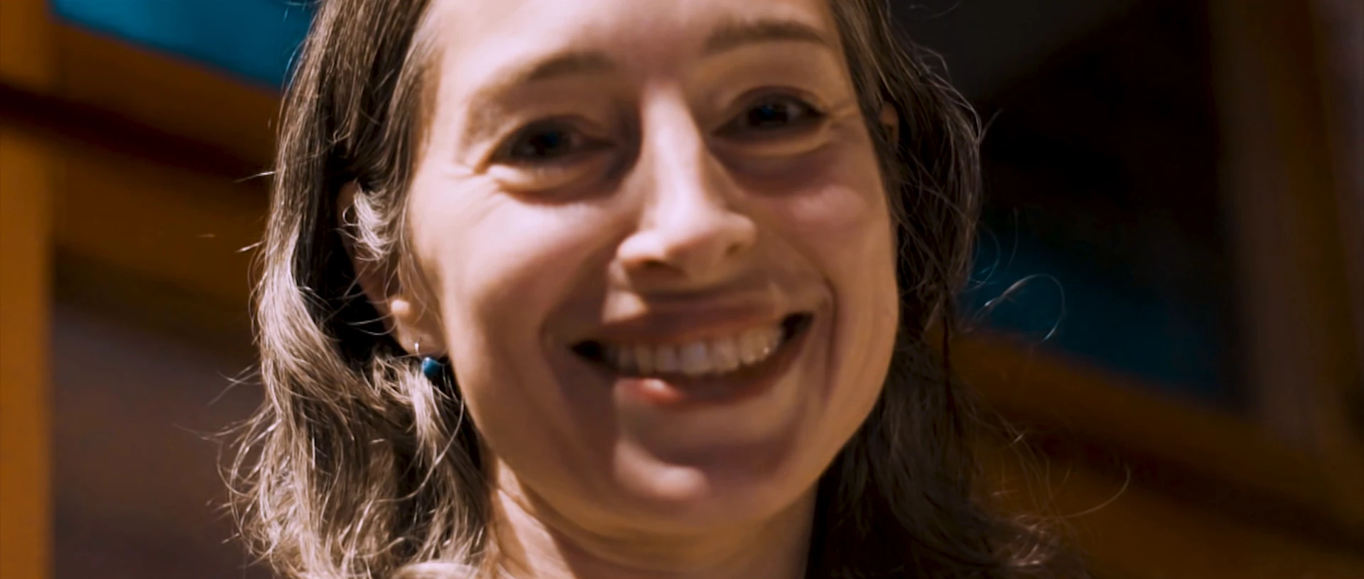 A woman with long hair smiles broadly at the camera in warm light.