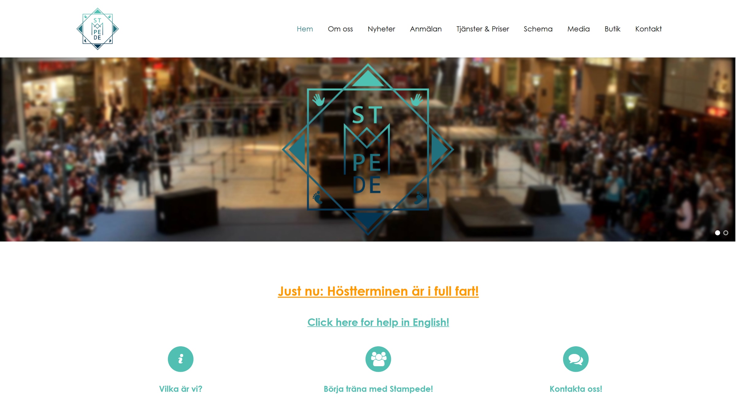 The Stampede website: the logo in blue at the top left next to the menu, and a large blue logo over a blurred photo of an audience in a shopping centre.